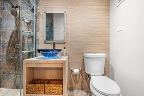 A bathroom with a glass bowl sink, a toilet, a shower, and a wooden vanity with baskets. - Quiet studio by the beach (San Juan)