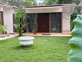 Una casa con techo de tejas, puerta principal oscura y un pequeño jardín con una maceta decorativa blanca.