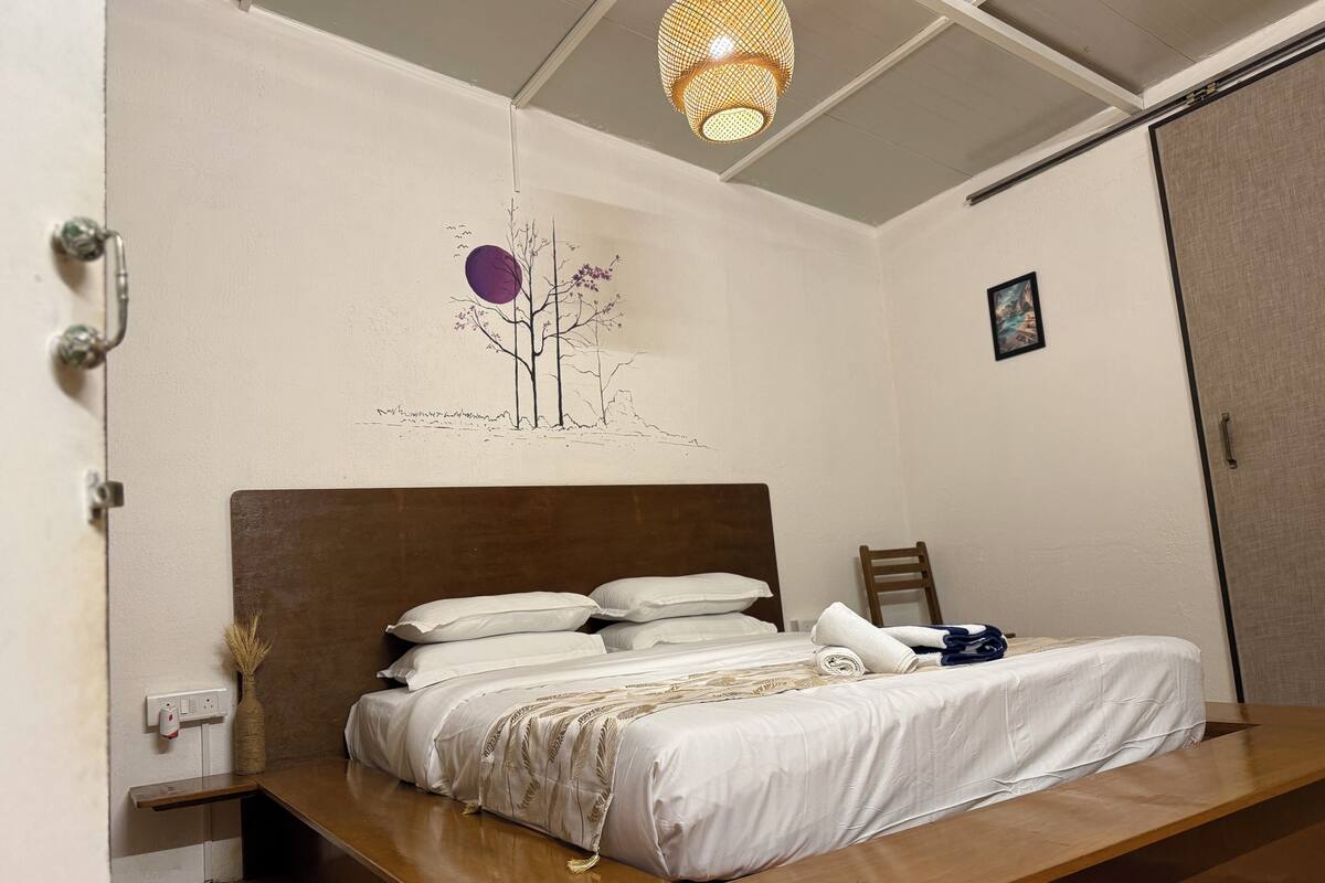 A bedroom with a bed, a nightstand, a wall-mounted light fixture, and a door.