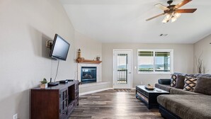 A living room with a television, fireplace, sofa, and a view through the door. - Beach House | Oceanfront + Fenced Yard (Crescent City)