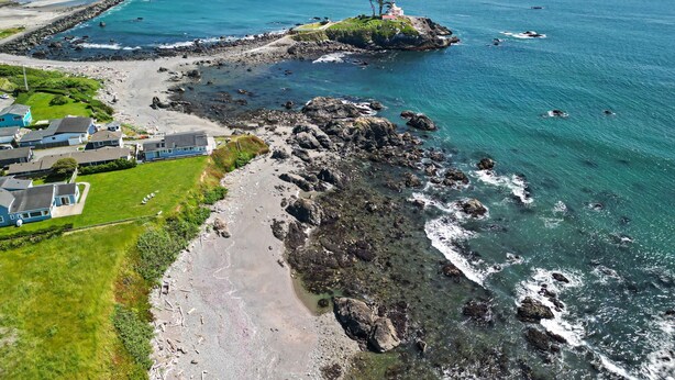 An aerial view of a coastal area with rocky terrain, a lighthouse, and a small island with a building. - Beach House | Oceanfront + Fenced Yard (Crescent City)