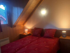 A bedroom with a sloped ceiling, two bedside tables with lamps, a bed with red bedding, and a window. - 3rd floor, fitness, swimming pool, sauna, balcony, parking, tv, ski locker, 70m², Saint Gervais (Saint-Gervais-les-Bains)