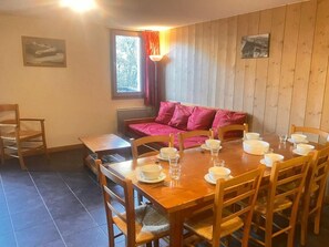 A dining area with a wooden table set for four, chairs, a sofa, and a window with curtains. - 3rd floor, fitness, swimming pool, sauna, balcony, parking, tv, ski locker, 70m², Saint Gervais (Saint-Gervais-les-Bains)
