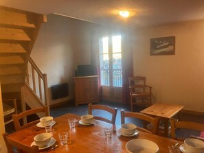 Ein Essbereich mit einem Holztisch, gedeckt für vier Personen, einer Holztreppe, einem Fernseher und einem Fenster mit Blick.