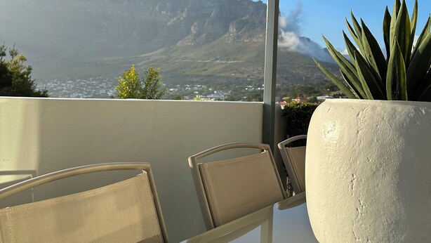 Un balcon donnant sur une chaîne de montagnes, une plante en pot et une table avec des chaises.