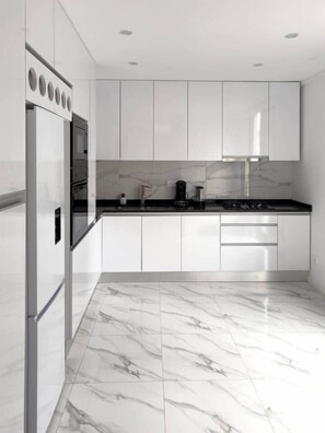 Une cuisine moderne avec des meubles blancs, un plan de travail noir et un sol en marbre.