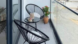 Uma varanda com porta de vidro, uma mesinha com cadeiras e plantas em vasos sobre prateleiras.