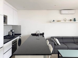 Une cuisine moderne avec un îlot central, un canapé gris et une petite table.