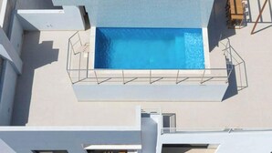 Una piscina en la azotea con superficie de agua azul cristalina, rodeada por un solárium blanco y una barandilla de metal.