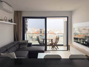 Un salon moderne comprenant un canapé, une table à manger avec des chaises et une grande porte-fenêtre coulissante donnant sur un balcon extérieur.