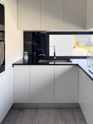 Une cuisine moderne avec un dosseret en marbre noir, un évier en acier inoxydable et des meubles blancs.