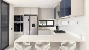 Een moderne keuken met witte kasten, een centraal eiland met barkrukken en een groot raam.