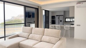 Een moderne woonkamer met een modulaire bank, een eethoek met witte stoelen, en een keuken op de achtergrond.