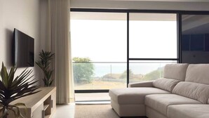 Een moderne woonkamer met een hoekbank, een flatscreen televisie, een houten dressoir en een groot raam met uitzicht.