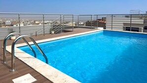 Ein Pool auf dem Dach mit Metallgeländer, einer Holzterrasse und weiter Aussicht auf die Stadt im Hintergrund.