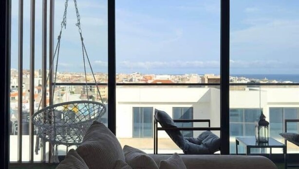 Ein modernes Wohnzimmer mit einer großen Couch, einem Hängesessel und Blick auf die Stadt durch große Fenster.