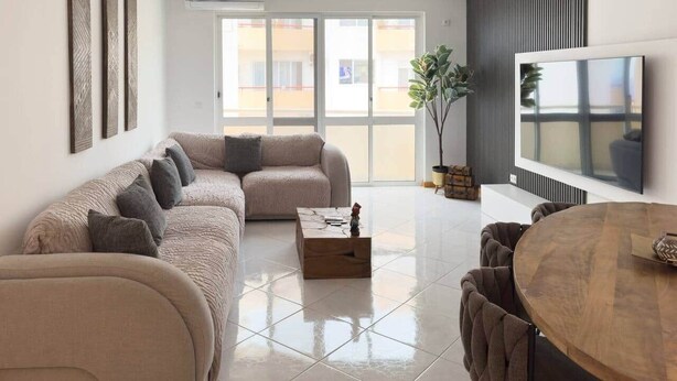 Ein modernes Wohnzimmer mit einer Eckcouch, einem Couchtisch, einem Esstisch und einem Fernseher.
