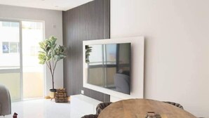 Ein modernes Wohnzimmer mit Holztisch, bequemen Sitzmöglichkeiten, einem wandmontierten Flachbildfernseher und einer Topfpflanze.