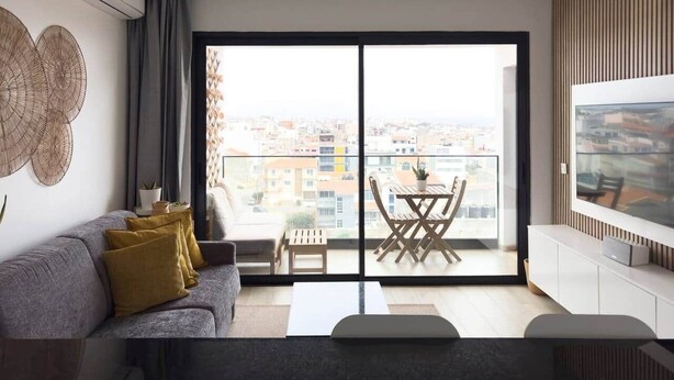 A modern living room with a sofa, a coffee table, and a TV on a wall. There's a balcony with a table and chairs. - 2 bdr aprt, stunning view,  rooftop pool - LCGR (Praia)