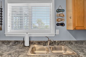 A kitchen with a double sink, a window with blinds, and wall decorations including signs. - C 22 Sundown Condominiums (Perdido Key)