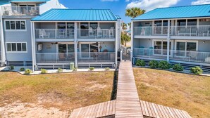 Ein Strandhotel mit zweistöckigen Gebäuden, Balkonen und einer Holzterrasse, die zum Eingang führt.