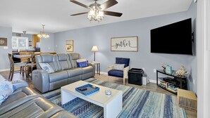 Ein modernes Wohnzimmer mit Sofa, Sesseln, Couchtisch, Fernseher und Deckenventilator.