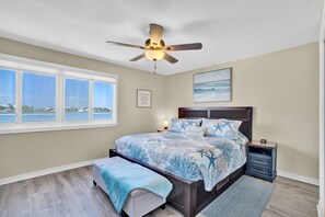 Ein Schlafzimmer mit einem Bett, einem Nachttisch, einem Deckenventilator, einem Fenster mit Blick und einem gerahmten Zitat an der Wand.