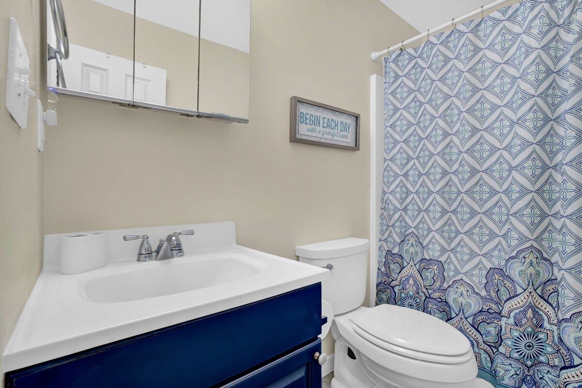 Ein Badezimmer mit weißem Waschbecken, einem blauen Schrank, einer Toilette und einem waschbär-gemusterten Duschvorhang.
