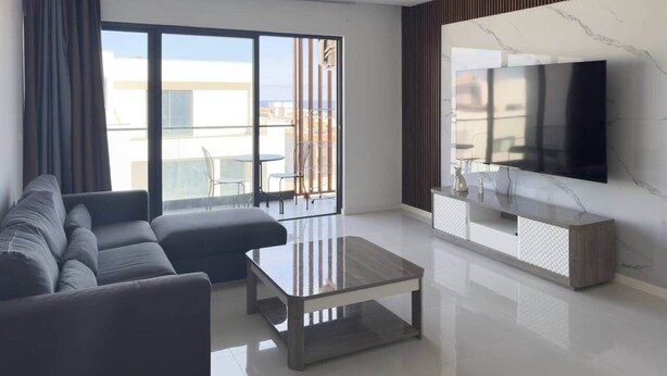 Ein modernes Wohnzimmer mit einer Couch, einem Couchtisch, einem Fernseher und einem Balkon mit Blick.