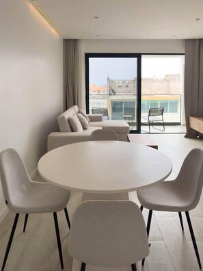 Una sala moderna con una mesa redonda y cuatro sillas, un sofá, y un balcón con vistas.