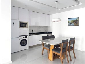Una cocina moderna con armarios blancos, un microondas integrado, una lavadora y un comedor con mesa y sillas.