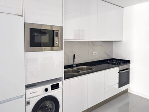 Cocina moderna con armarios blancos, microondas integrado, estufa a gas y pileta de acero inoxidable.