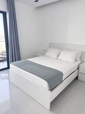 Un dormitorio moderno con una cama grande, una mesita de noche y un ventanal con cortinas.