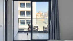 Quarto com porta de vidro deslizante que dá para uma varanda com duas cadeiras e uma mesa.