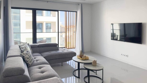 Uma sala de estar moderna com um sofá modular cinza, uma mesinha redonda e uma televisão de tela plana na parede.
