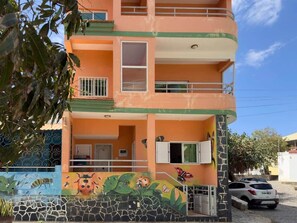 A multi-story building with balconies, a mural with ladybugs and butterflies, and a car parked in front.