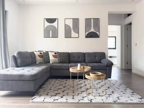 A modern living room with a grey sectional sofa, two round wicker side tables, and abstract wall art.