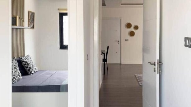 Moderni hotellihuone, jossa on sänky, pieni oleskelualue ja käytävä, joka johtaa ovelle.