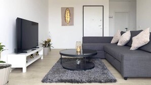 A modern living room with a flat-screen TV, a round coffee table, a grey sofa, and a white console table. - Spacious 2 bdr aprt, rooftop pool - LCGR (Praia)