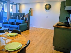 A modern living room with a blue sofa, a dining table with green plates, and a kitchen area with a sink and countertop. - LUX T2 Calm, Modern & Cosy - Caen Centre (Caen)