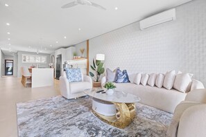 A modern living room with a sofa, a coffee table, and a dining area in the background.