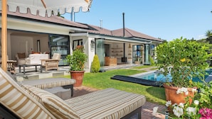 Ein modernes Haus mit Swimmingpool, Sitzgelegenheit im Freien und einem gepflegten Garten.