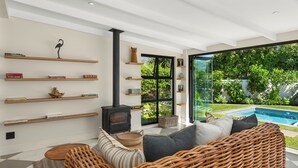 Ein modernes Wohnzimmer mit Kamin, Korbmöbeln und Blick auf einen Swimmingpool.