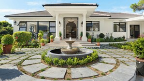 Ein Haus mit einem runden Steinbrunnen, einem überdachten Eingang und einem Garten mit Kübelpflanzen.