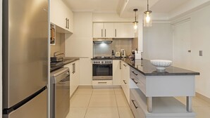 A modern kitchen with stainless steel appliances, a central island, and pendant lighting. - Beachfront Apartment | Table Mountain Views (Cape Town)