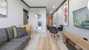 A modern living room with a grey sofa, wooden coffee table, and a TV on the wall. - Stylish 2BR @ The Onyx | Rooftop Pool and Braai (Umhlanga)