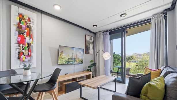 A modern living room with a glass dining table, black chairs, a wooden bench, a sofa, and a TV. - Stylish 2BR @ The Onyx | Rooftop Pool and Braai (Umhlanga)