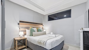 A bedroom with a bed, bedside table, lamp, and a window. - Stylish 2BR @ The Onyx | Rooftop Pool and Braai (Umhlanga)
