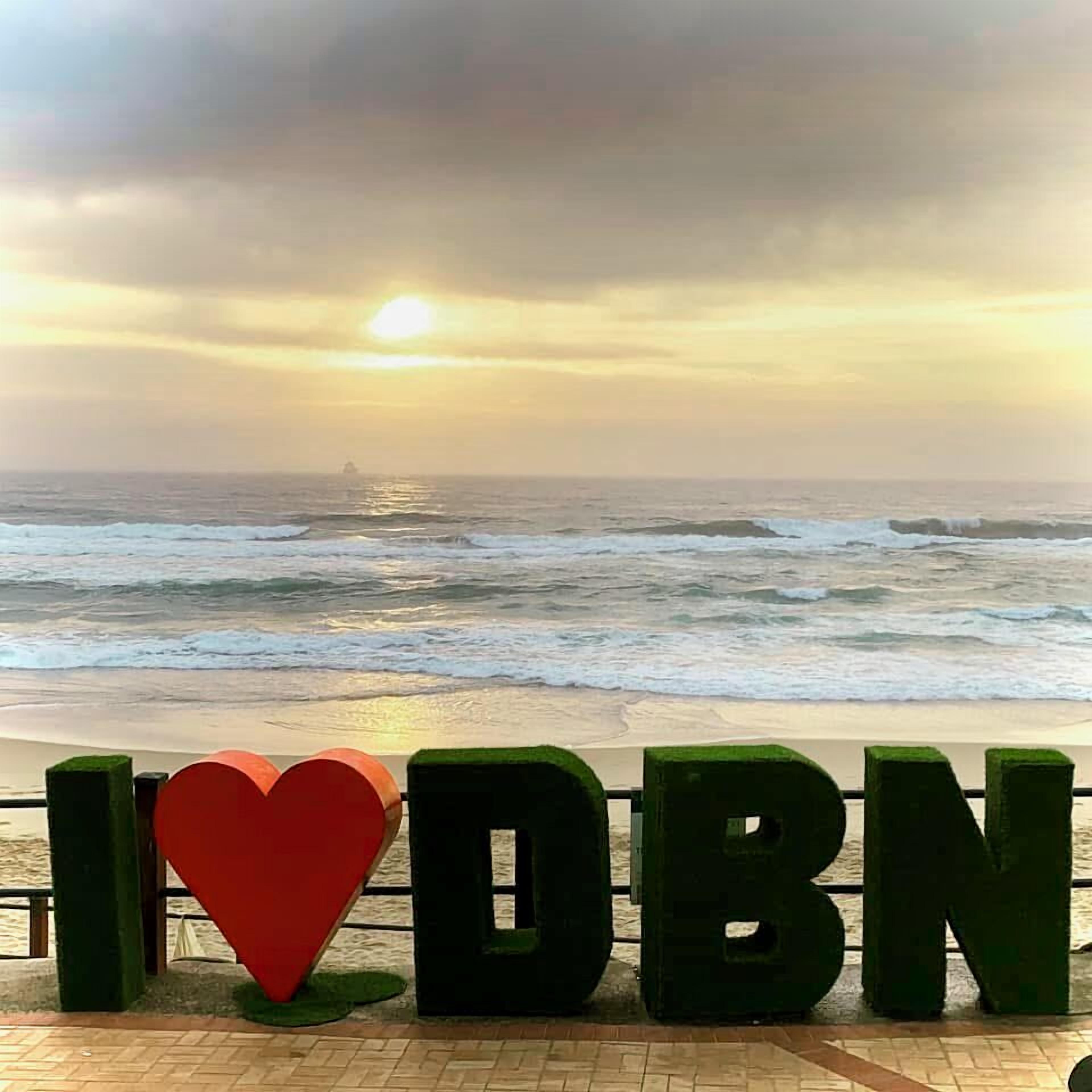 A beach view with a sign spelling 'I ❤️ DBN' and waves in the background.