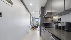 A modern kitchen with a dishwasher, a sink, and a dining area with chairs. - Stylish 2BR @ The Onyx | Rooftop Pool and Braai (Umhlanga)